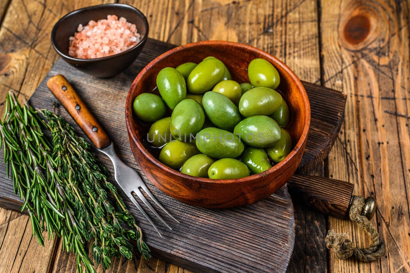 Marinated Green big olives in wooden bowl with oil. wooden background. Top view by Composter