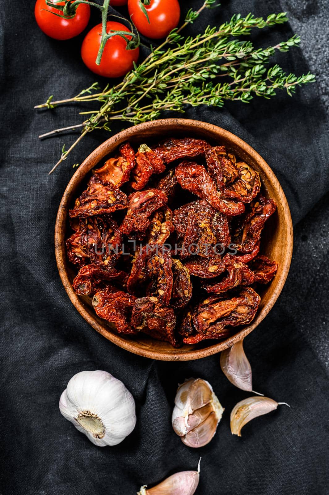 Dried tomatoes with garlic, spices and herbs. Recipe for cooking with ingredients. Black, dark background. Top view.