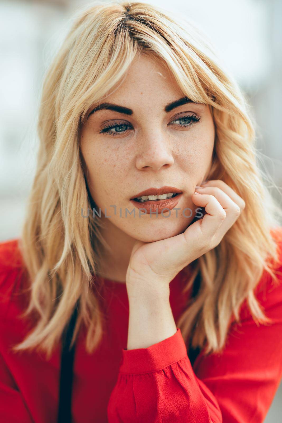 Attractive young blond woman sitting on urban background. Blonde girl with red shirt enjoying life outdoors.