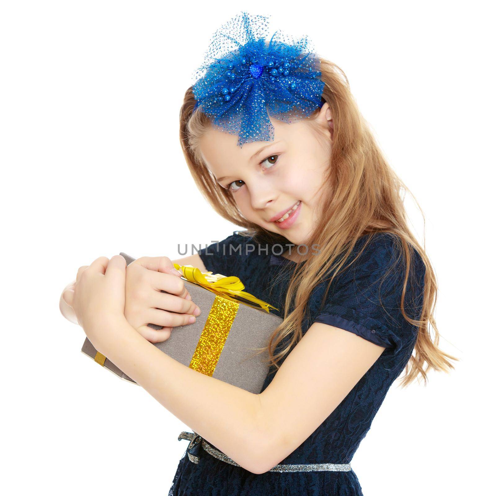 Cute Caucasian little girl In a dark blue dress and big blue bow on her head. The girl holds box with gift.Isolated on white background.