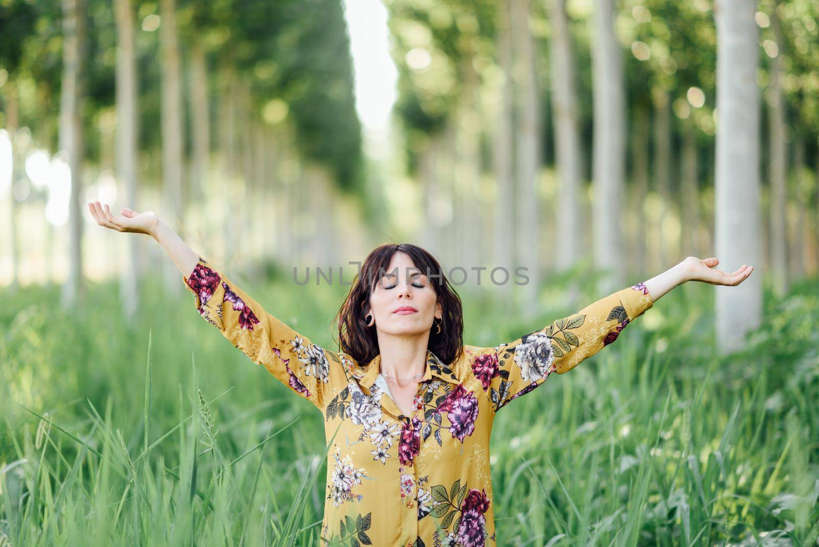 Enjoying the nature. Young woman arms raised enjoying the fresh air in green forest. Female with eyes closed.