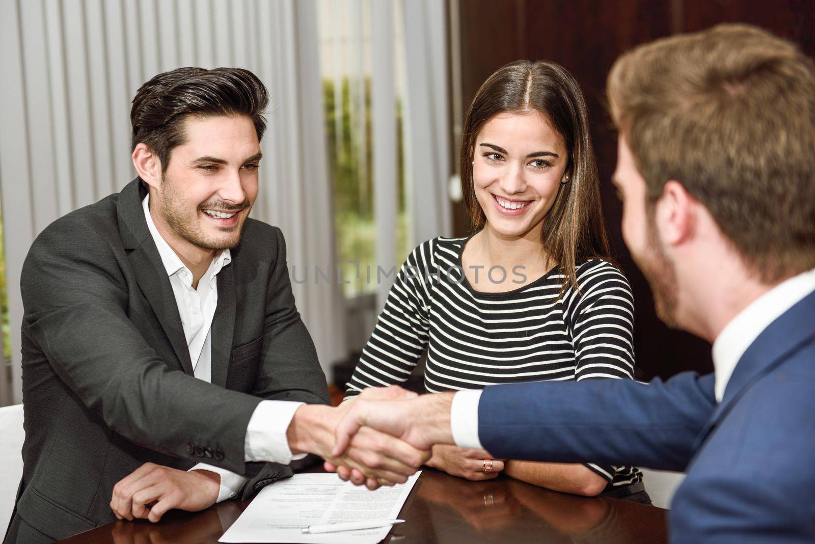 Smiling young couple shaking hands with an insurance agent by javiindy