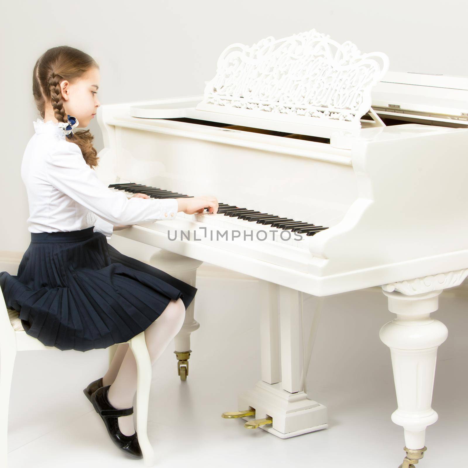Charming little blonde with long wattled hair in plaits, playing on a white grand piano. In musical school.