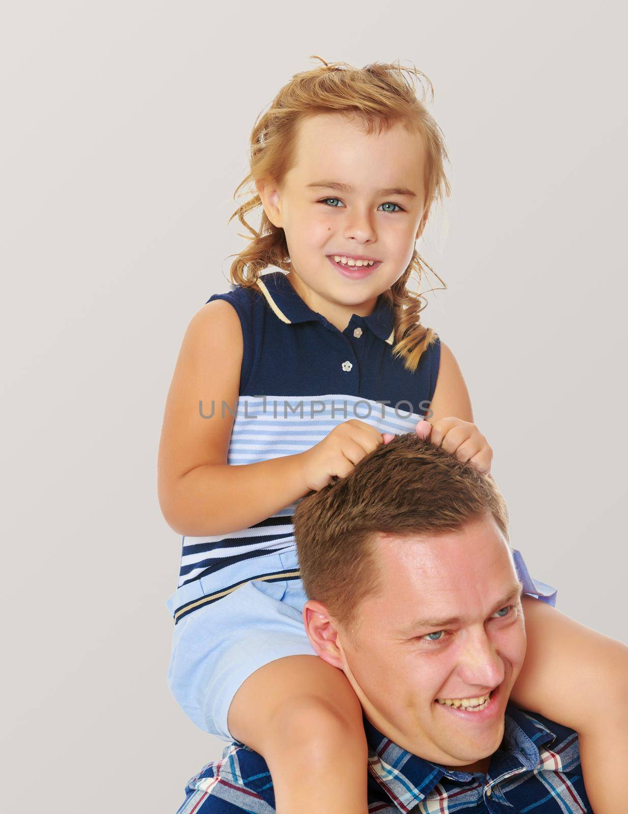 Happy little blond-haired, tanned girl sitting on the neck of the Pope.On a gray background.