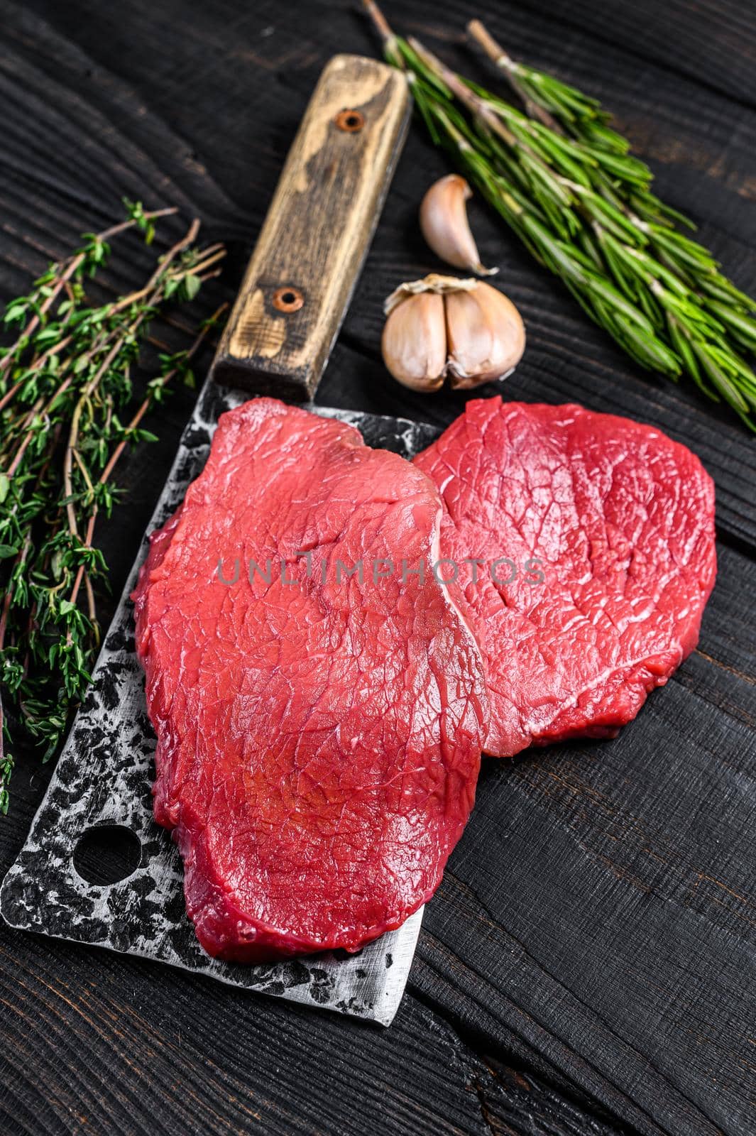 Raw marble beef meat fillet steak on butcher cleaver. Black wooden background. Top view.