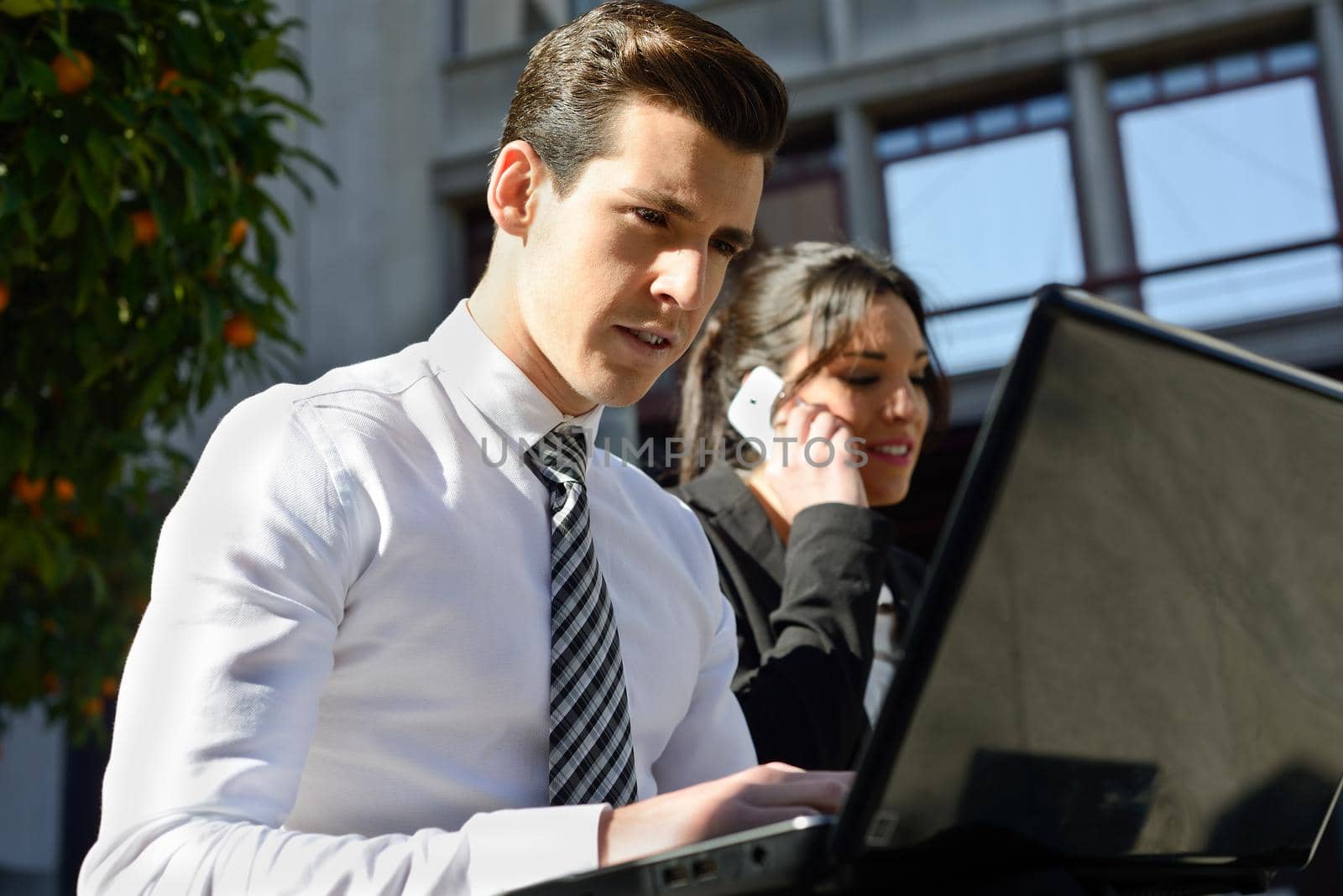 Portrait of attractive young businessman typing in a laptop computer in urban background