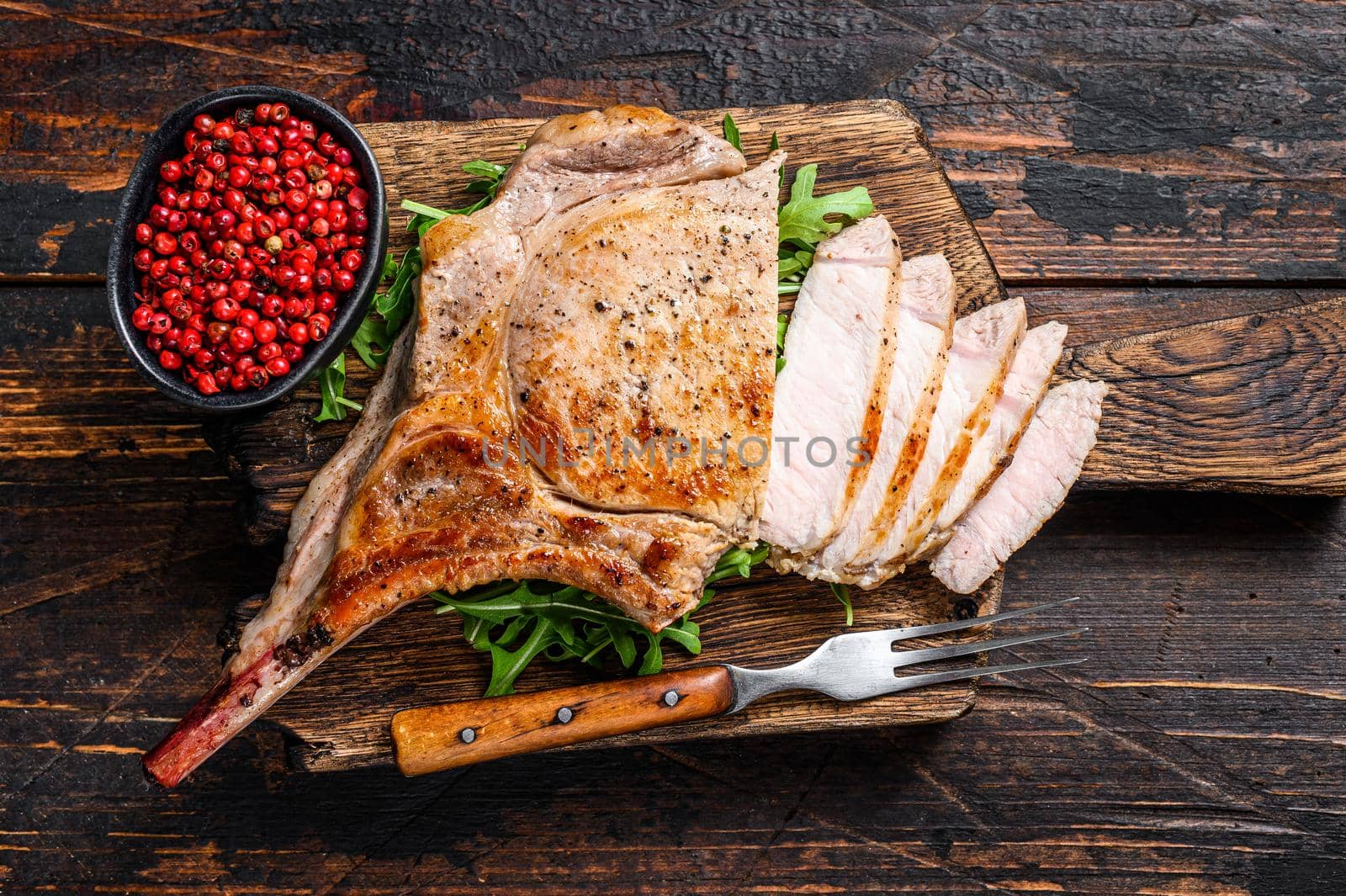 Grilled and sliced tomahawk pork chop meat steak on a marble board. Dark Wooden background. Top view by Composter