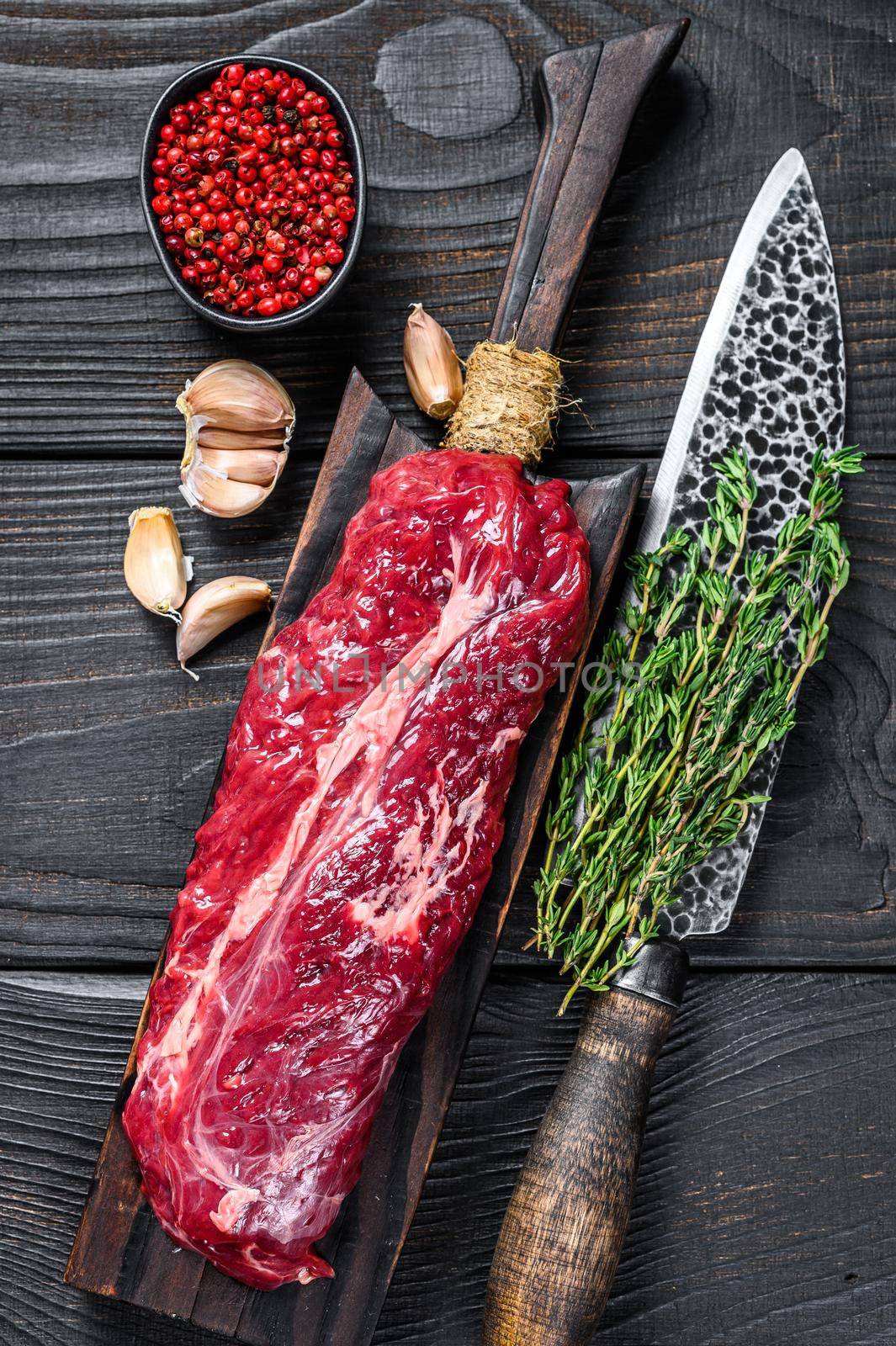 Raw Onglet Hanging Tender beef meat steak on a wooden cutting board. Black wooden background. Top view.
