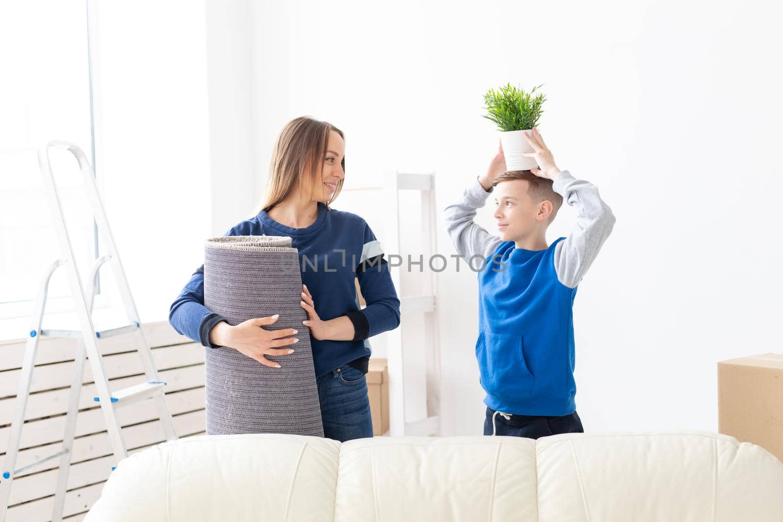 Young cute single mother and son are happy about the move to new house holding a pot of greens and carpet in their hands. Concept of housewarming and family space extensions. by Satura86