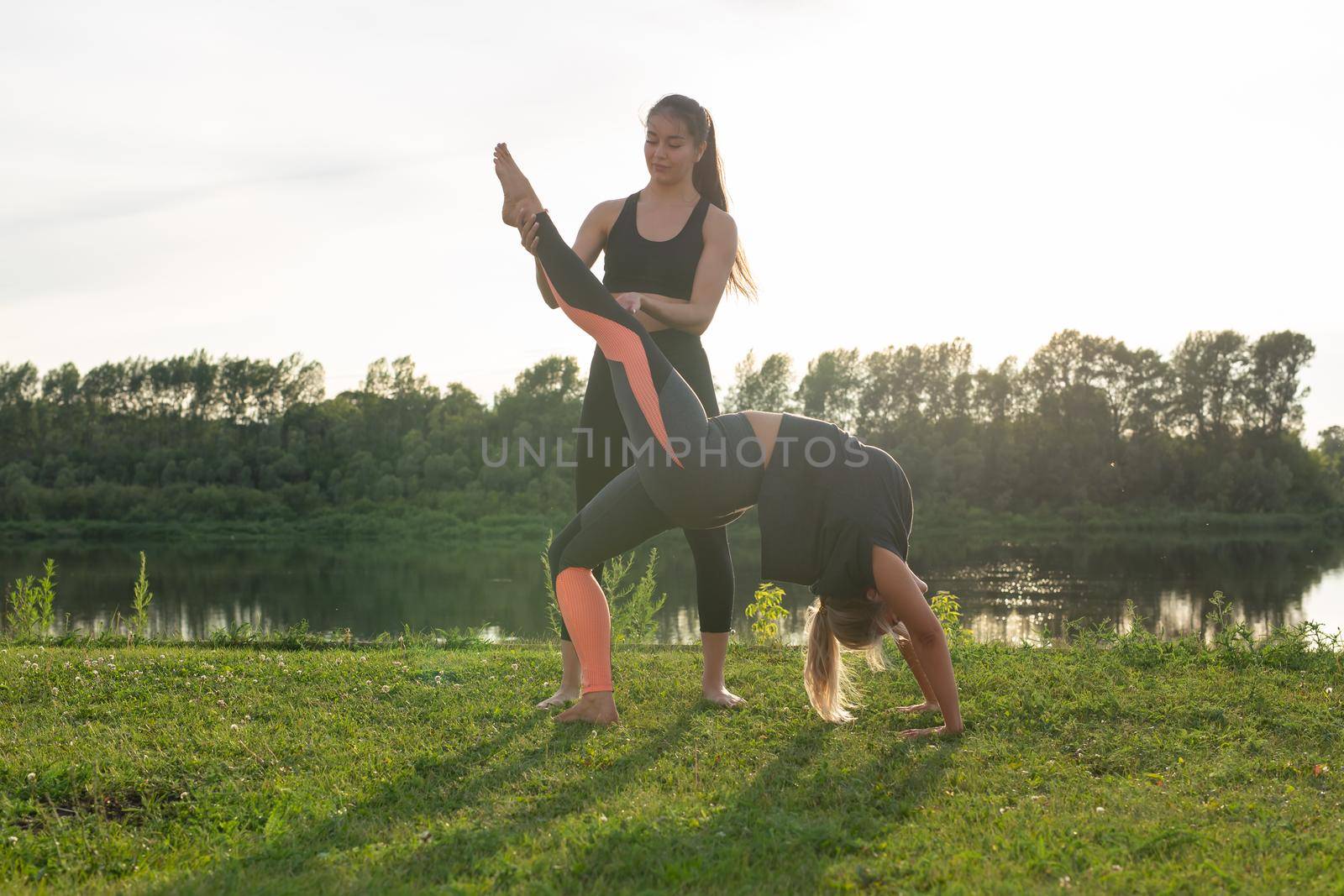 Harmony and healthy lifestyle concept - Young slim women in sportswear practicing yoga outdoors