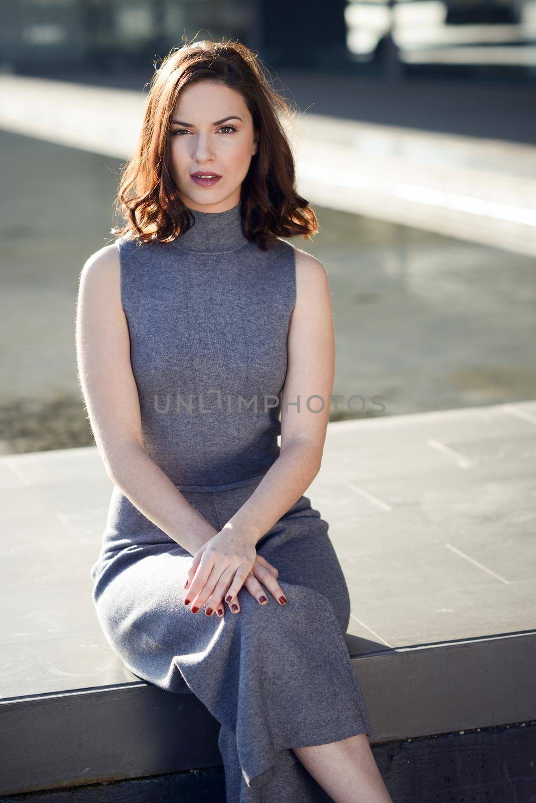 Beautiful young woman, model of fashion, sitting in urban background