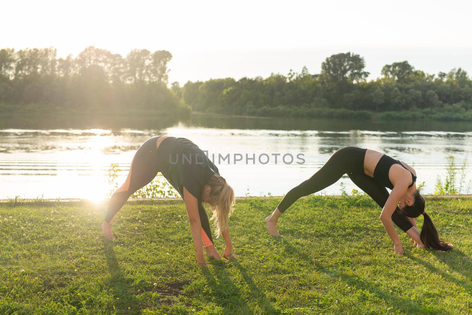 Harmony and healthy lifestyle concept - Young slim women in sportswear practicing yoga outdoors
