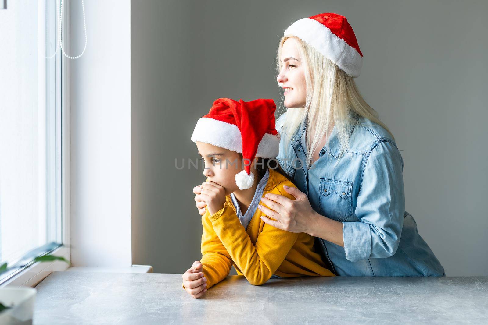 Adorable caucasian blond mom with daughter both wearing Santa caps by Andelov13