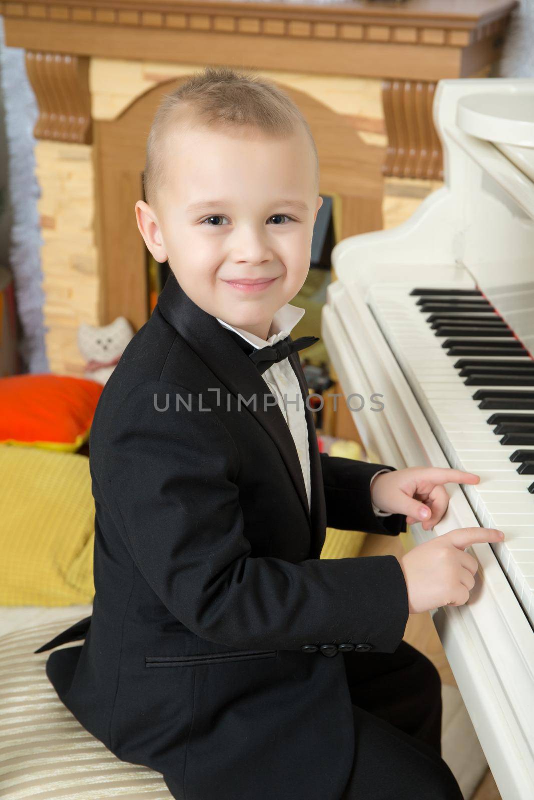 Beautiful little boy in a strict black suit , white shirt and tie.He sits at the piano keys.