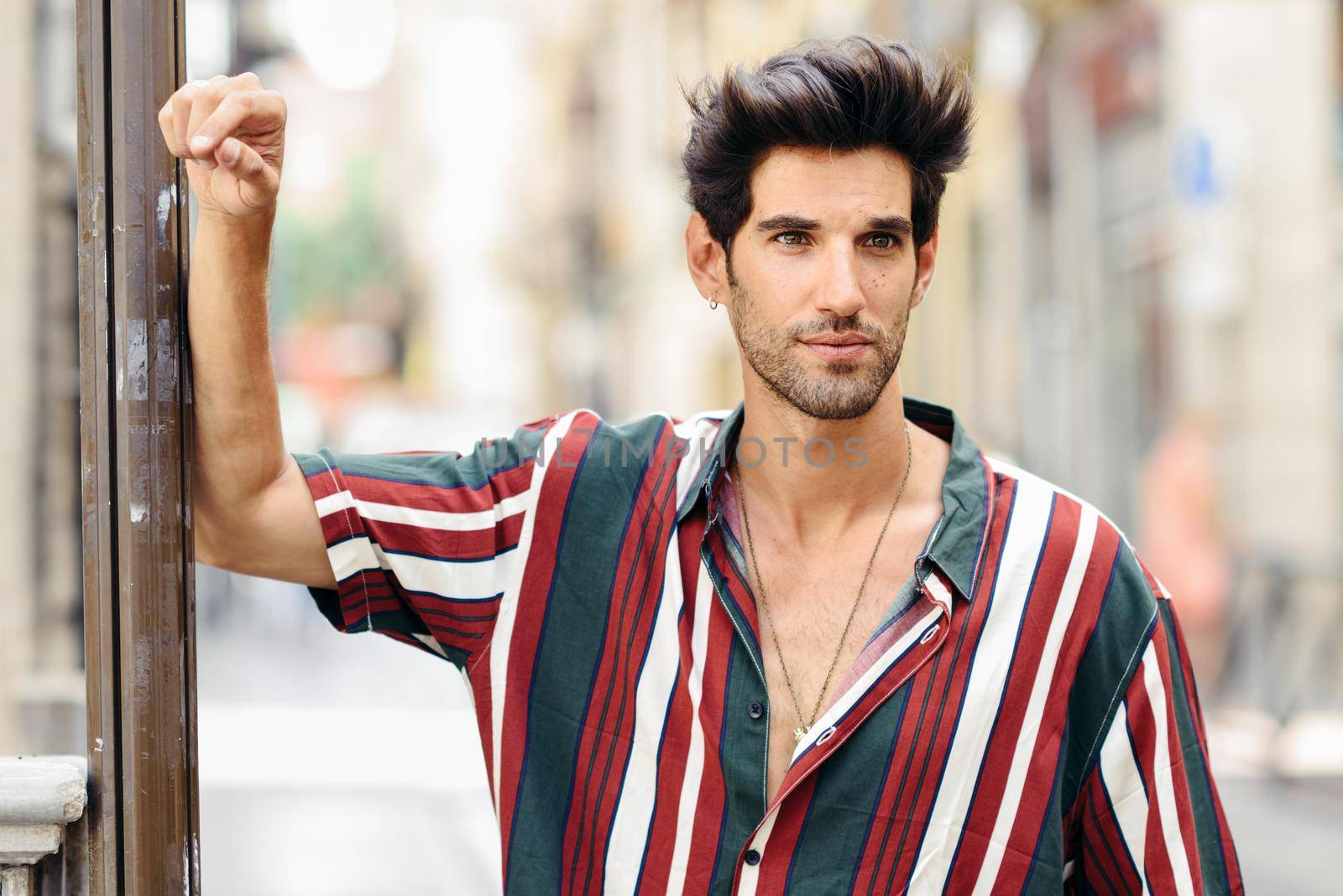 Attractive young man with dark hair and modern hairstyle wearing casual clothes in urban background. Guy with lost look.