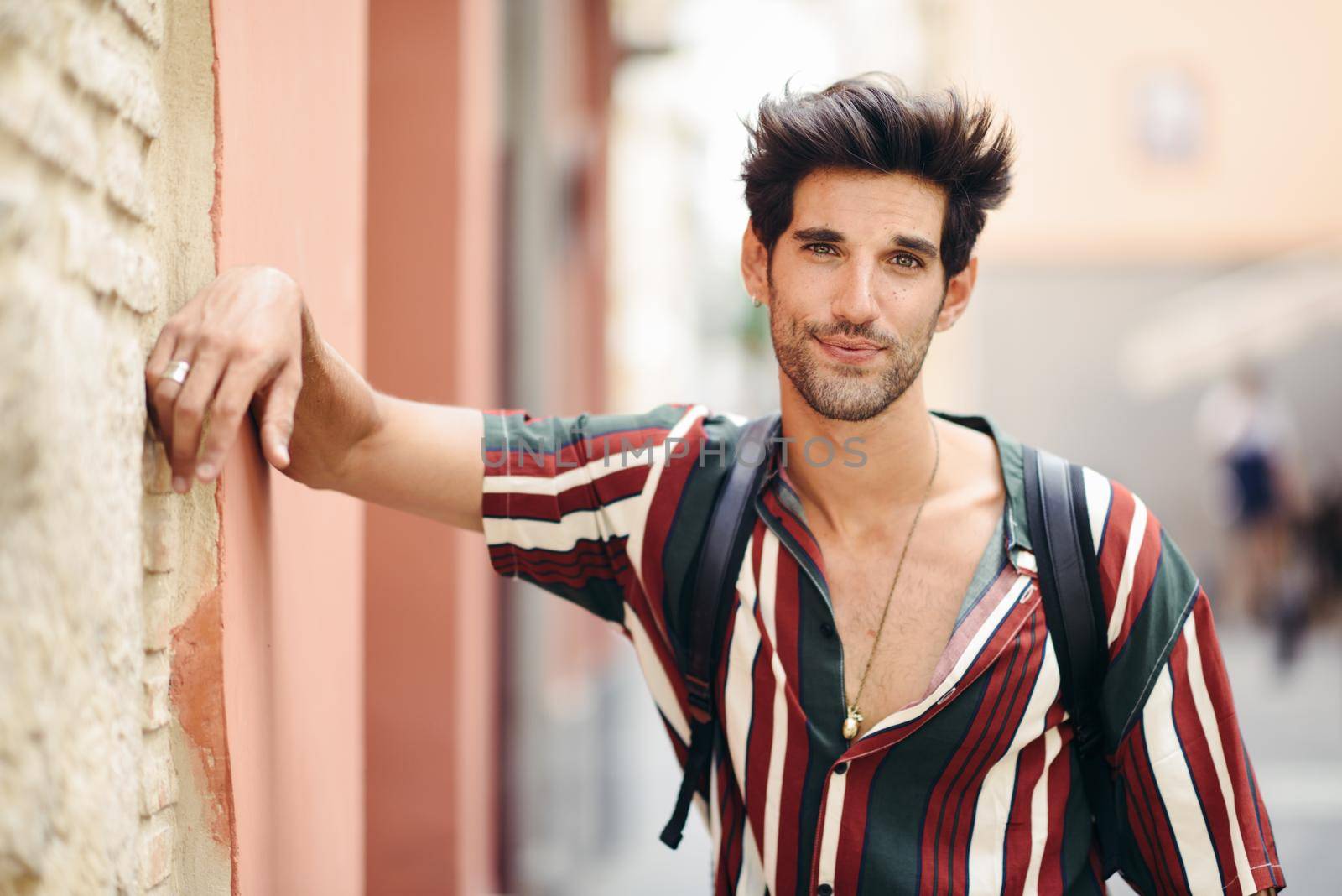 Handsome young man with dark hair and modern hairstyle wearing casual clothes in urban background.