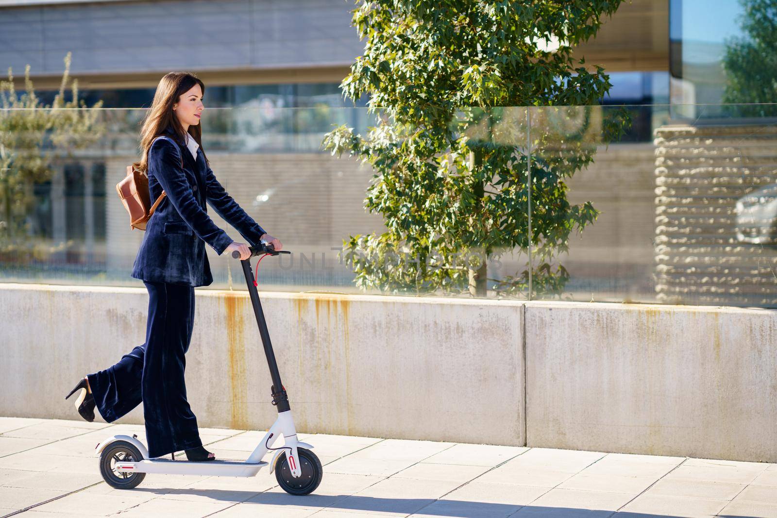 Young business woman wearing blue suit using electric scooter. Lifestyle concept.