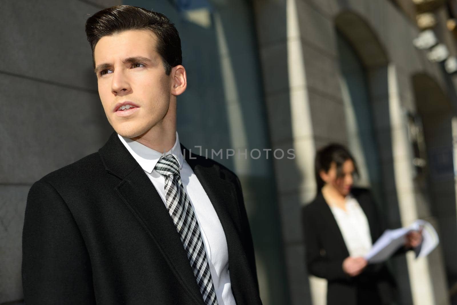 Portrait of attractive young businessman in the city with beautiful businesswoman in the background