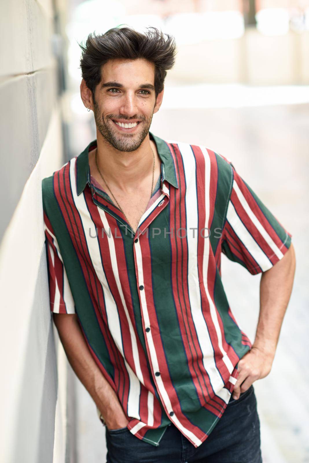 Attractive young man with dark hair and modern hairstyle wearing casual clothes in urban background.