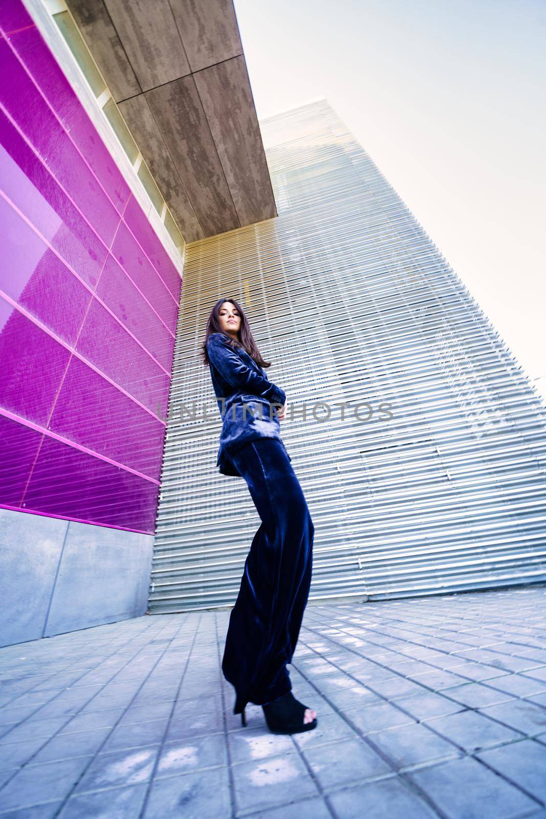 Wide-angle photo of a woman wearing blue suit posing near a modern building. Fashion concept.