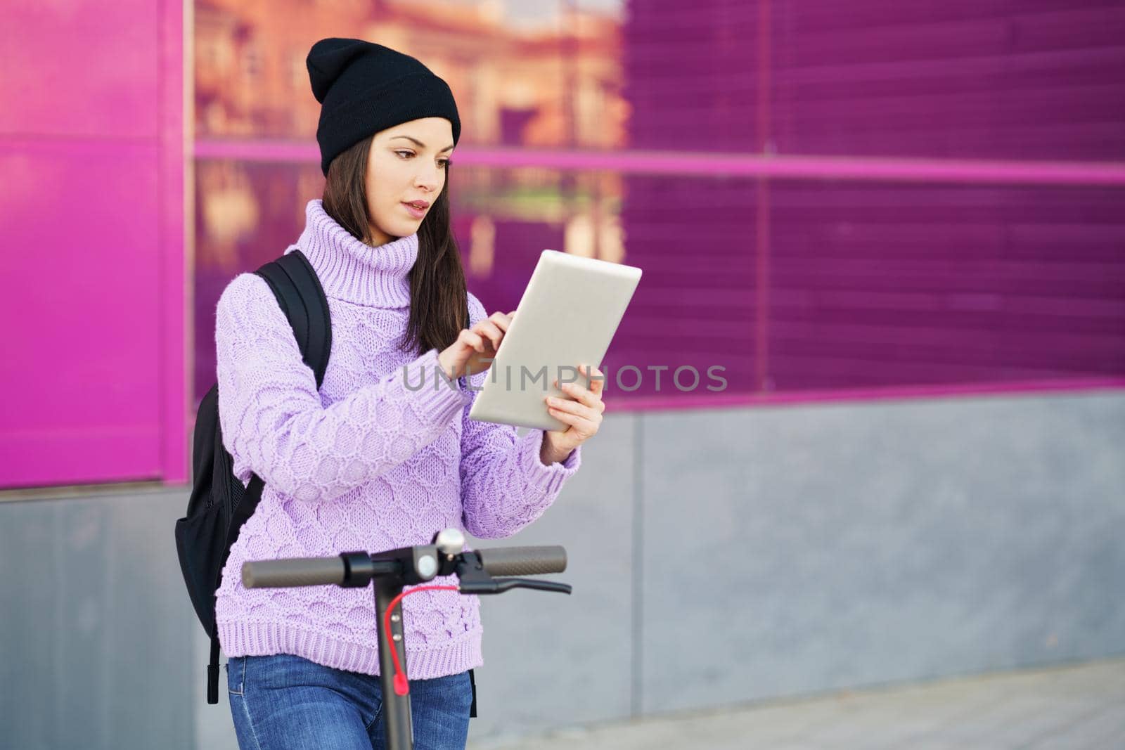 Woman in her twenties with electric scooter using digital tablet outdoors. Lifestyle concept.