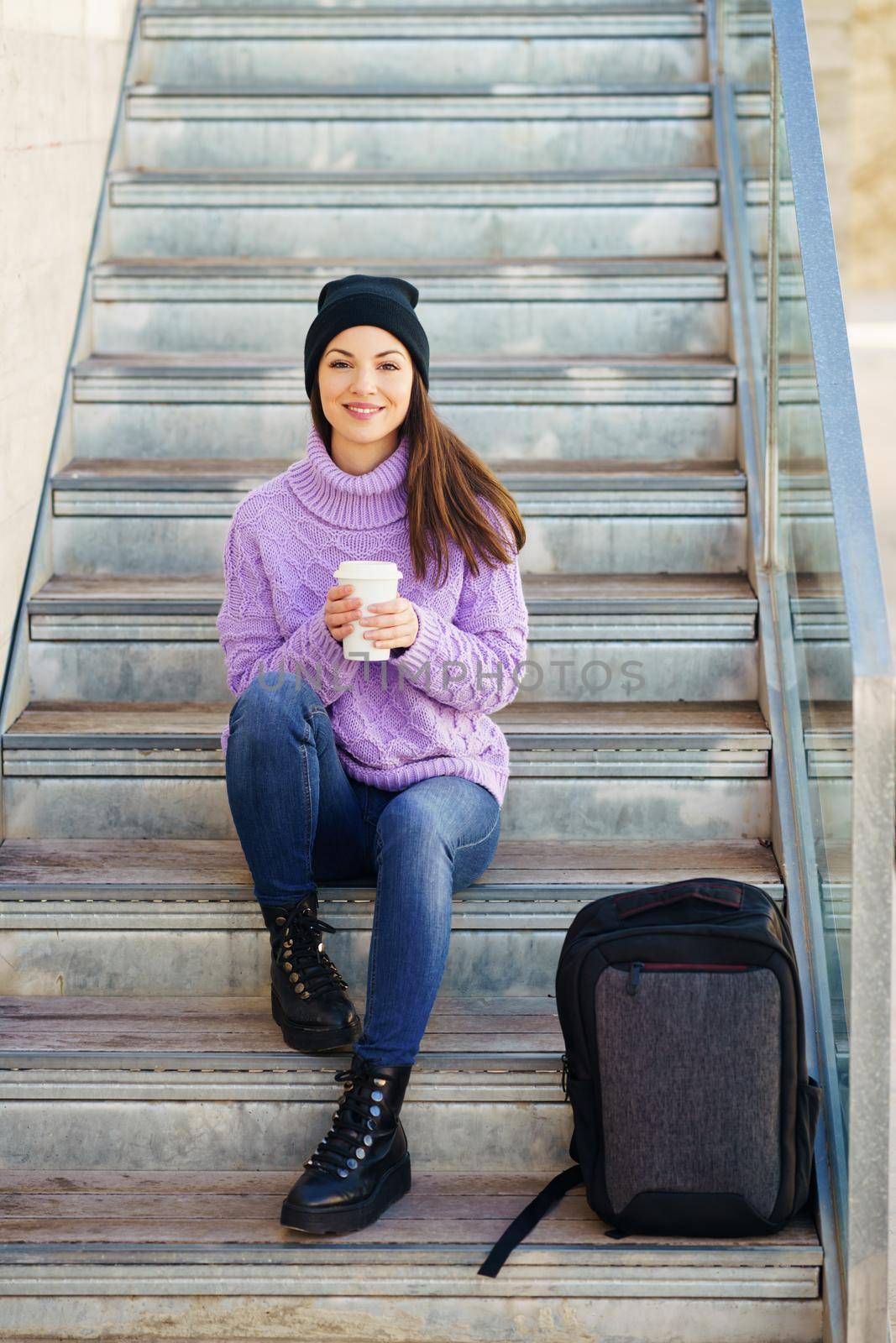 Woman in her twenties taking a coffee break sitting on some steps in the street. Lifestyle concept.