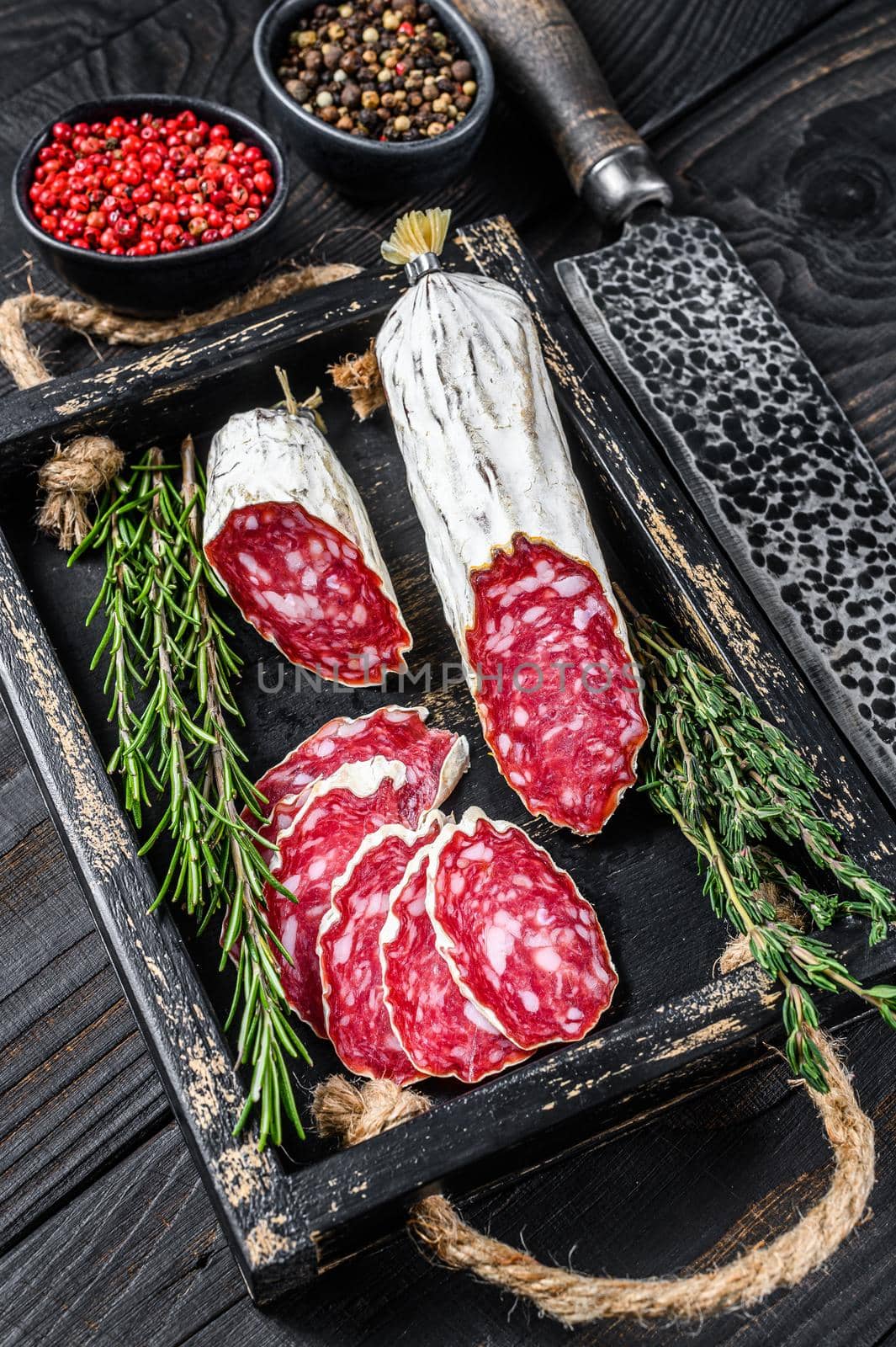 Slices of dry cured salchichon salami in a wooden tray. Black wooden background. Top view.