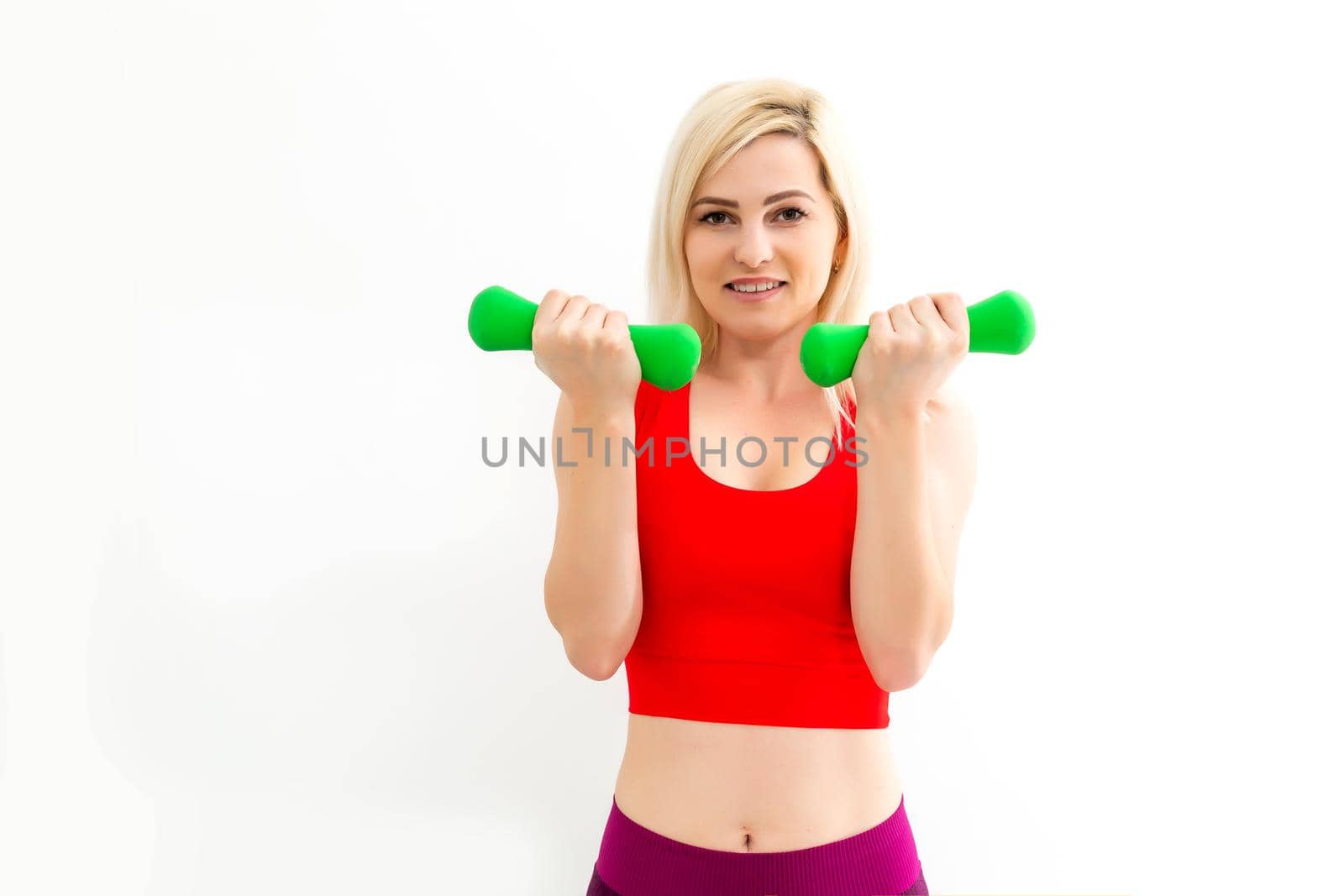 Smiling athletic woman pumping up muscles with dumbbells on white background