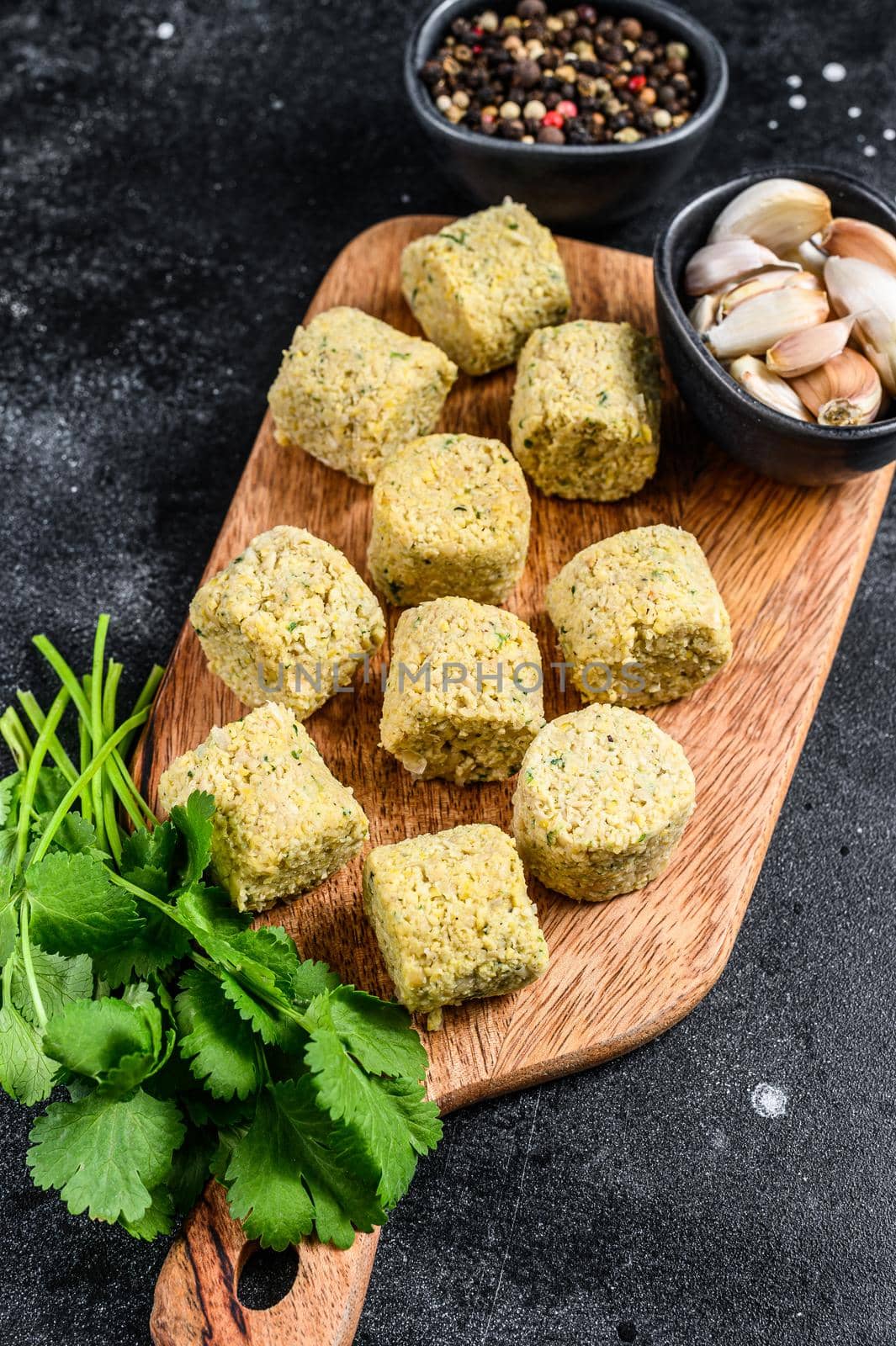 Raw falafel balls on a wooden cutting board. Black background. Top view by Composter