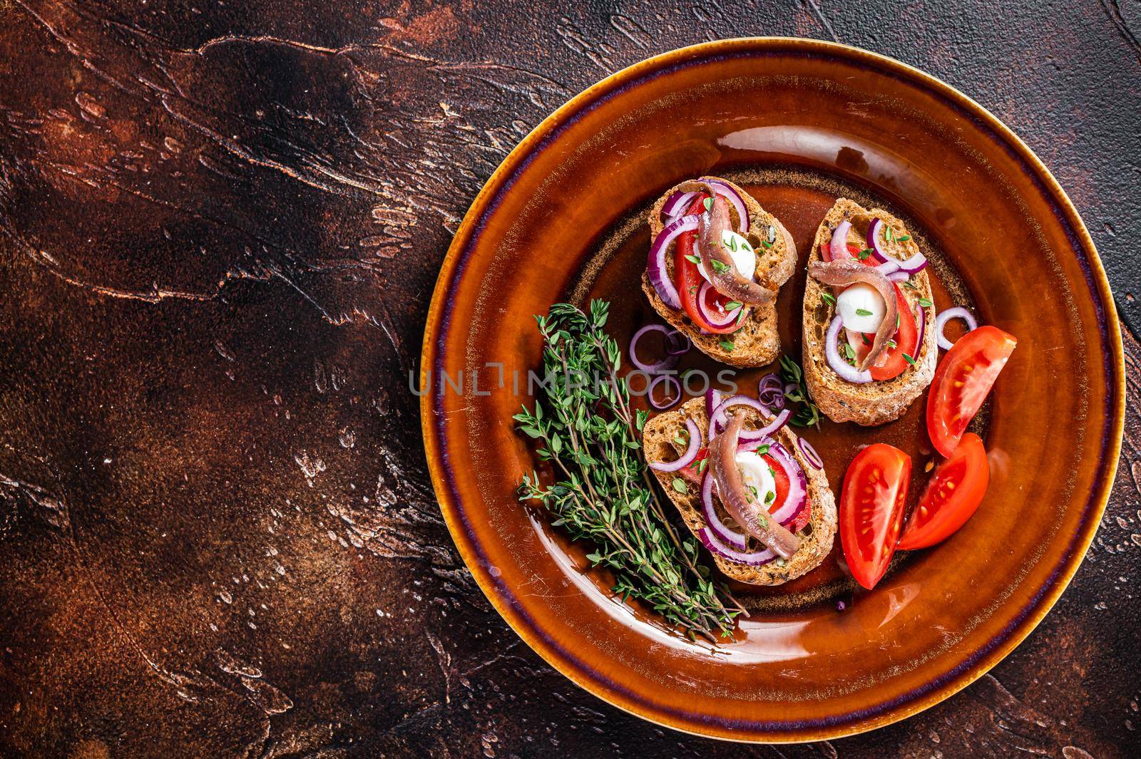 Spanish tapas on bread with olive oil, herbs, tomatoes and spicy anchovy fillets. Dark background. Top view. Copy space by Composter