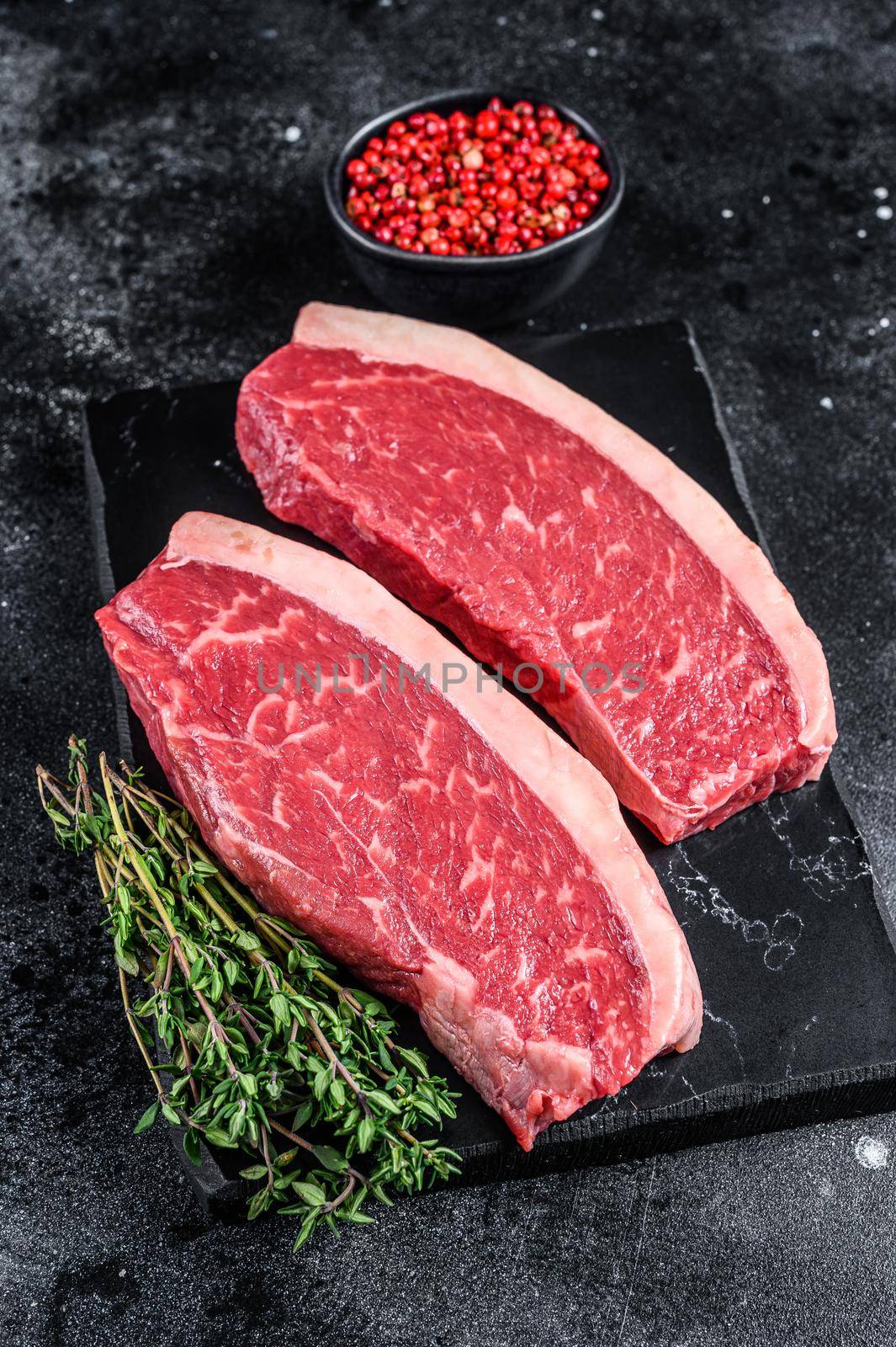 Raw cap rump steak or top sirloin beef meat steak on marble board. Black background. Top view by Composter