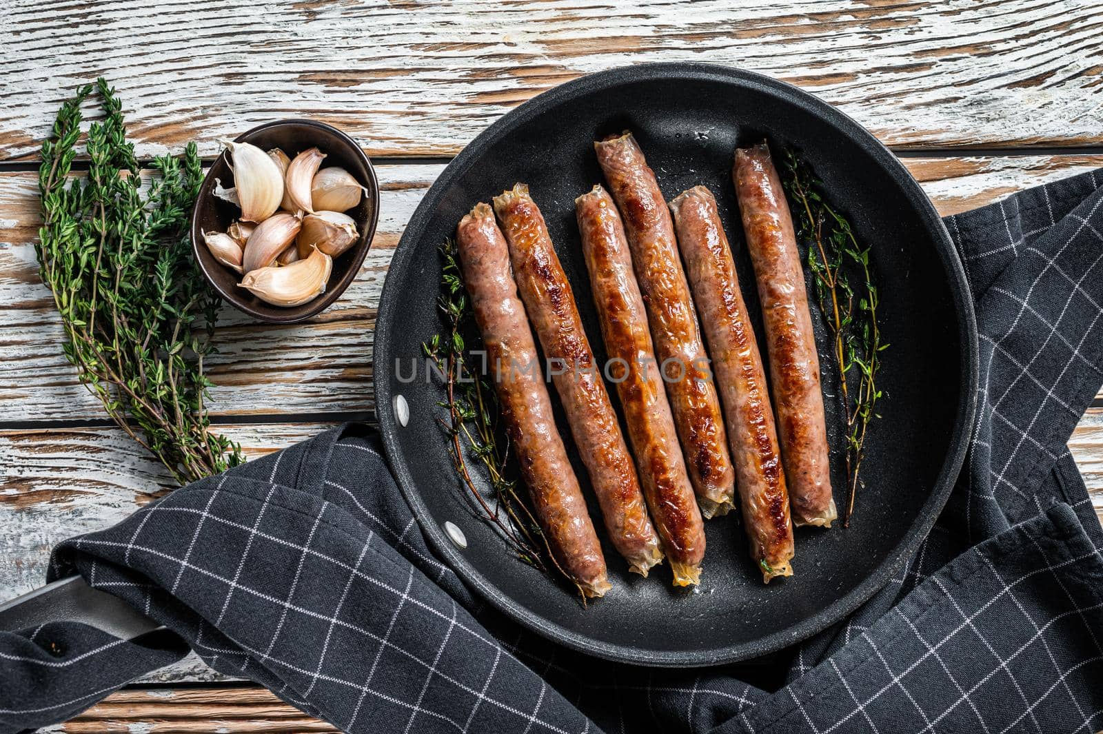 Fried beef and pork meat sausage in a pan with italian herbs and cheese. White wooden background. Top view.