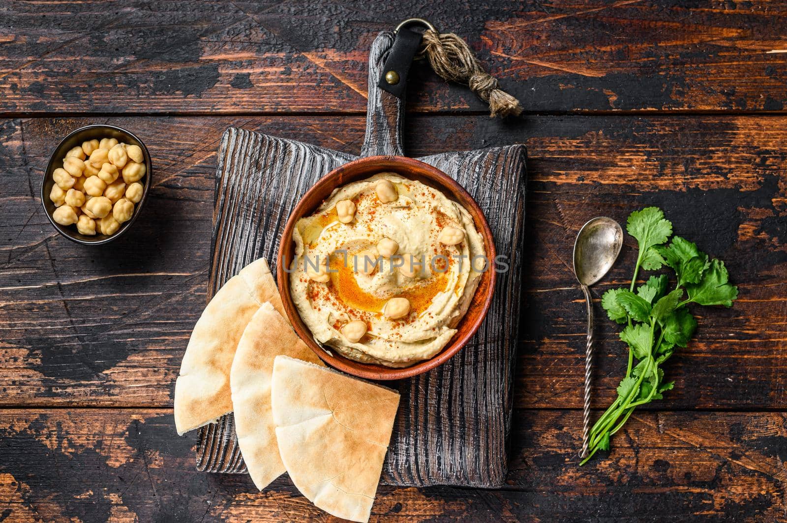 Hummus paste with pita bread, chickpea and parsley in a wooden bowl. Dark wooden background. Top view by Composter