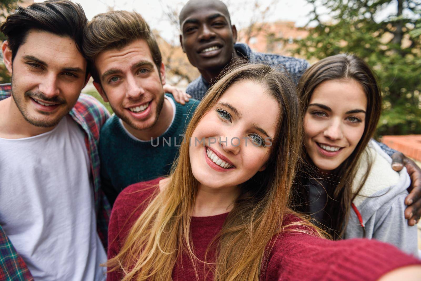 Multiracial group of friends taking selfie in a urban park with a blonde young girl in foreground