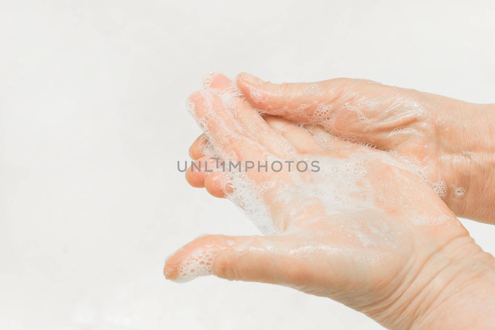 An adult woman's hands lathered with soap, close-up. Hand washing and domestic hygiene concept.