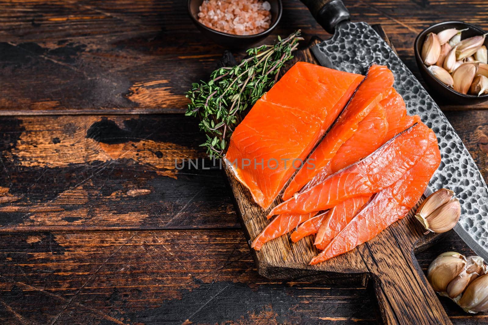 Sliced Smoked salmon fillet on a wooden cutting board with herbs. Dark wooden background. Top view. Copy space by Composter