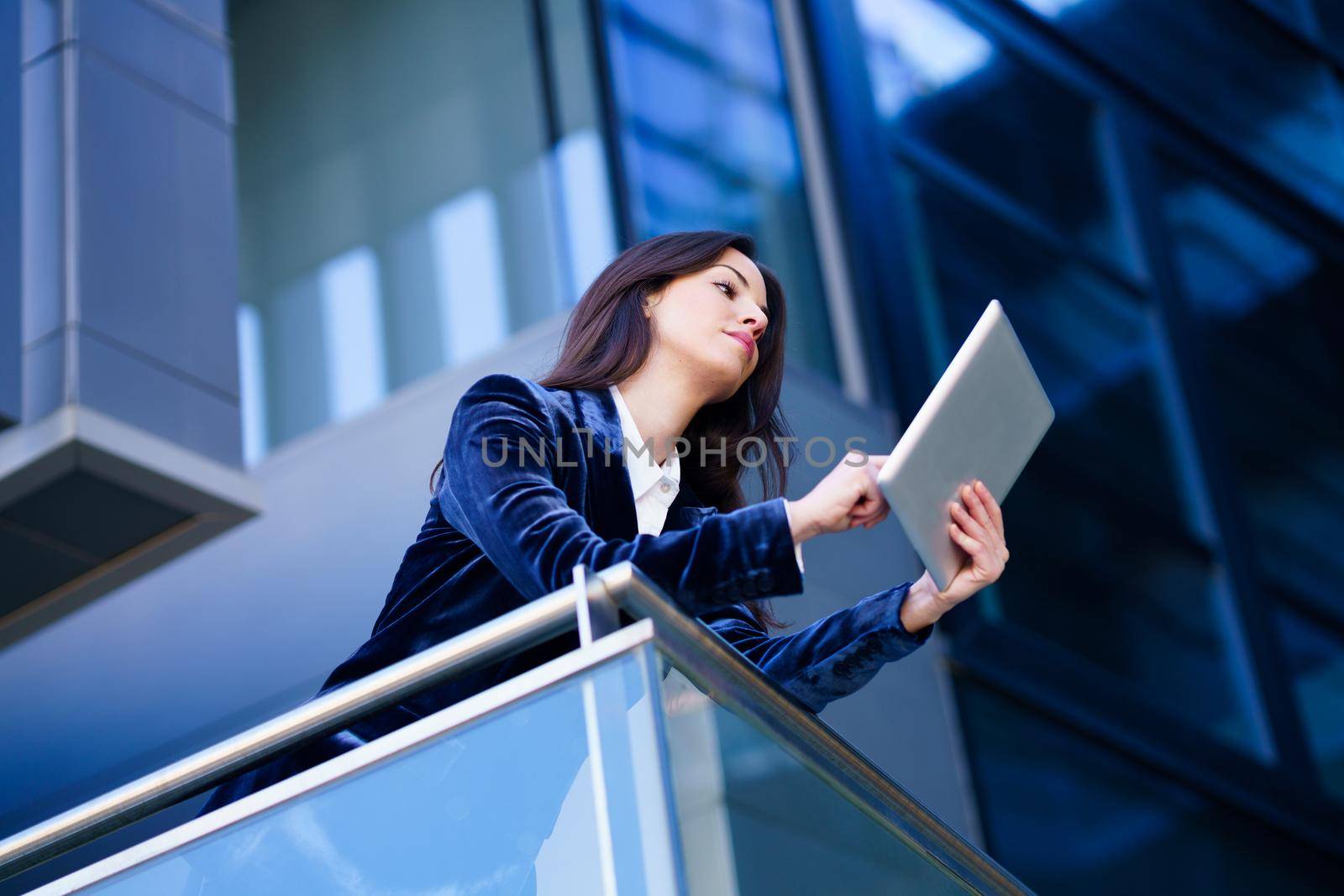 Business woman wearing blue suit using digital tablet in an office building. by javiindy