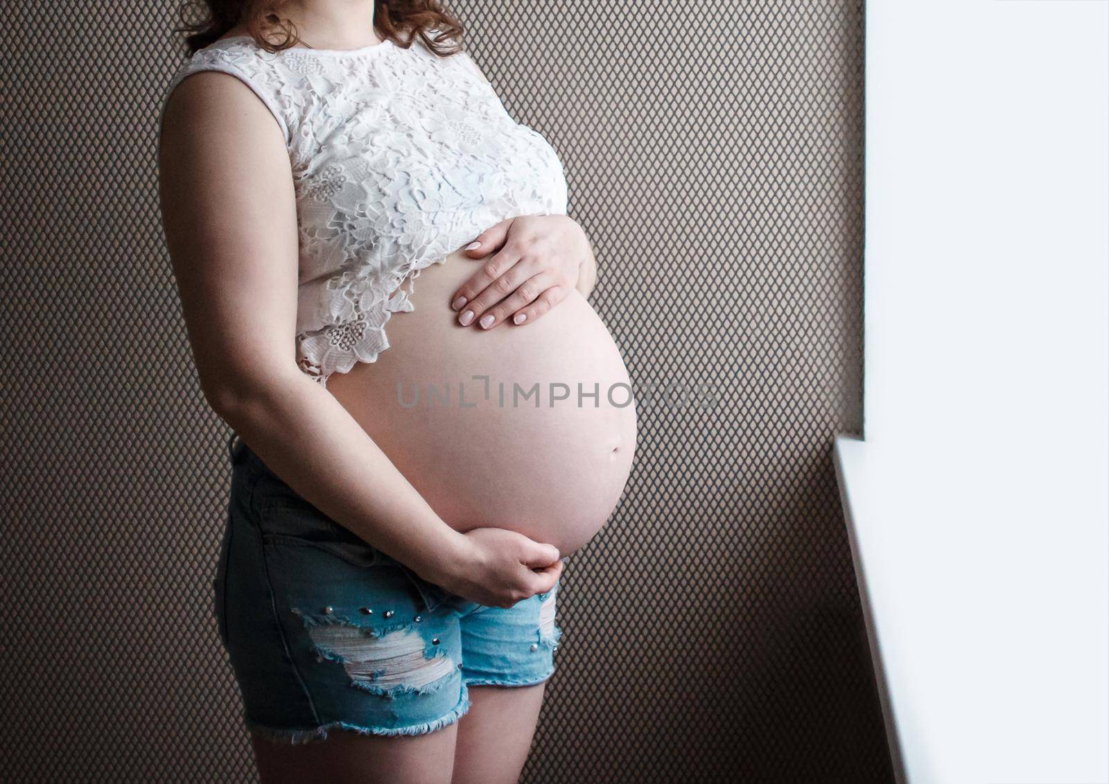 The hands of a pregnant girl hold their stomach, waiting for the birth of a child.