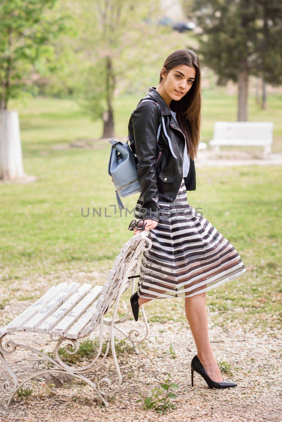 Portrait of young woman smiling in urban background wearing casual clothes. Girl wearing striped skirt, sweater and leather jacket