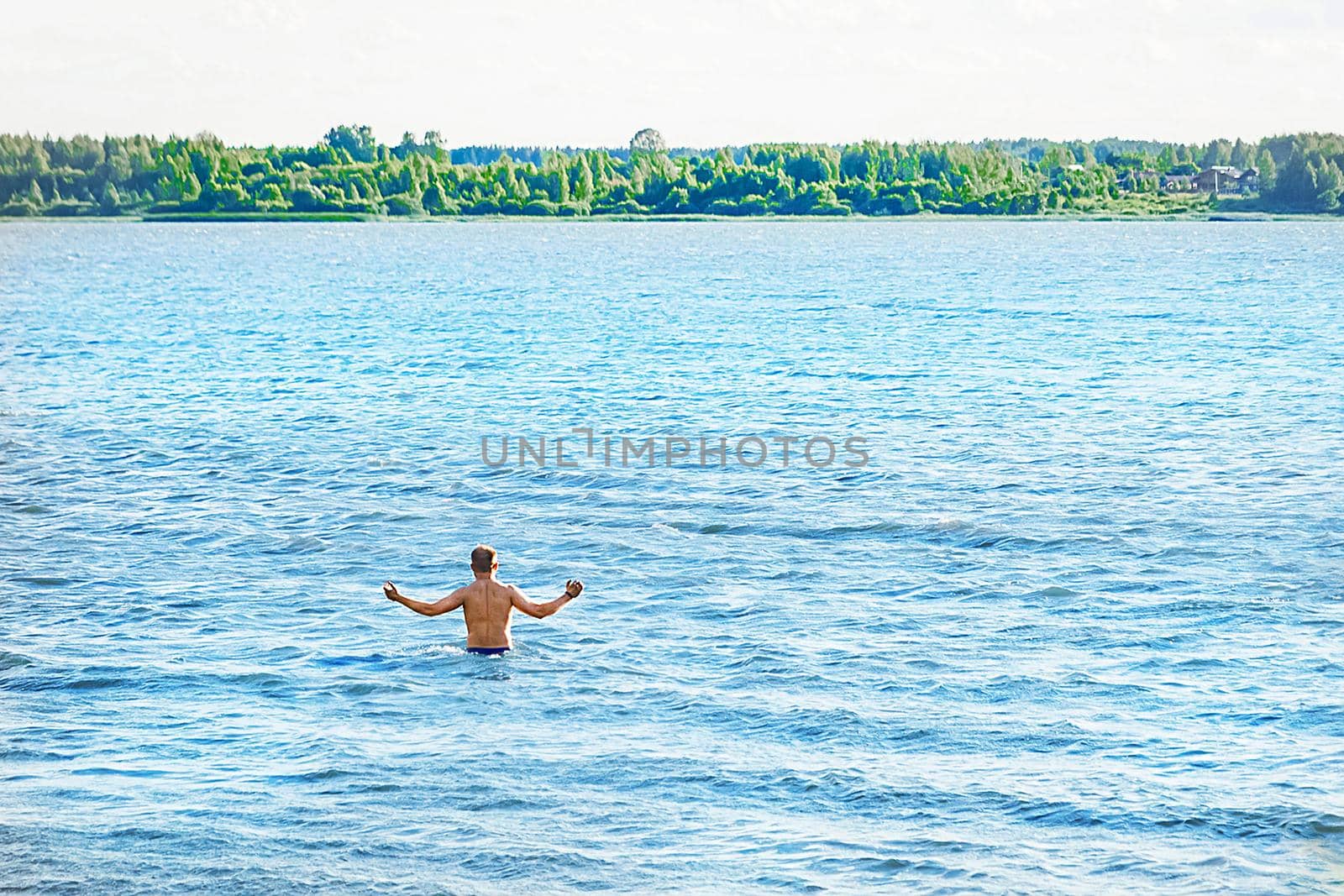 A man with a bare body has put his hands to the sides and is going to dive into the water of the lake in the open air, nature background.