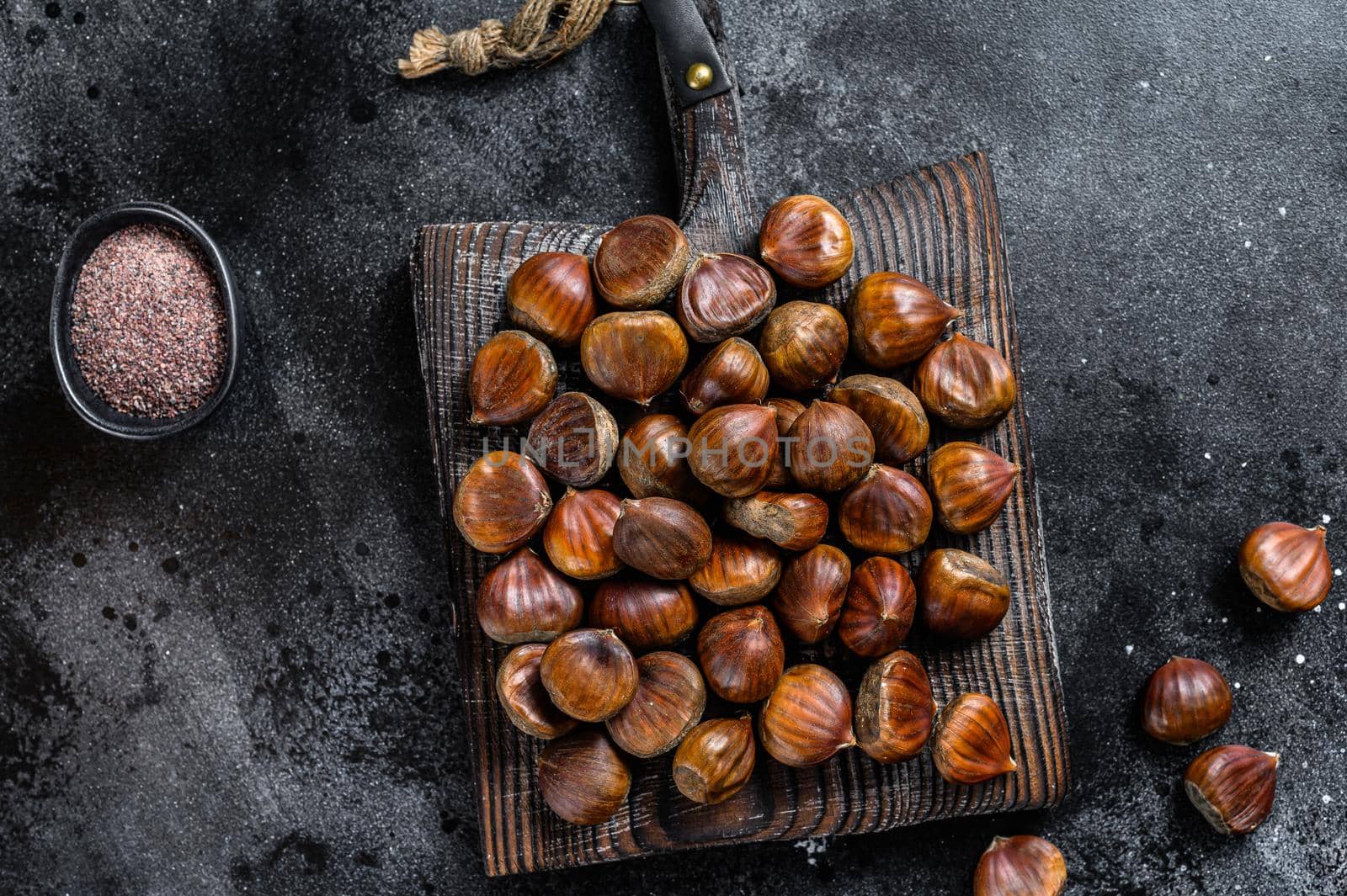 Raw chestnuts on a wooden cutting board. Black background. Top view by Composter