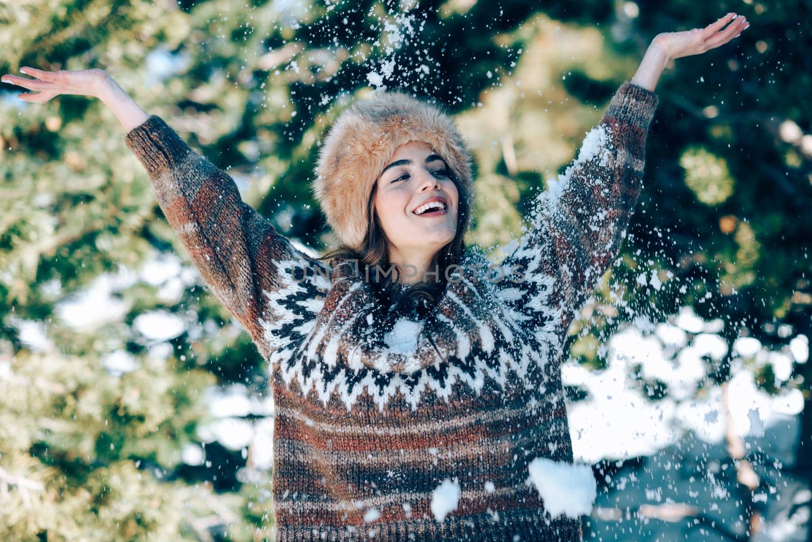 Young woman enjoying the snowy mountains in winter, in Sierra Nevada, Granada, Spain. Female wearing winter clothes playing with snow.