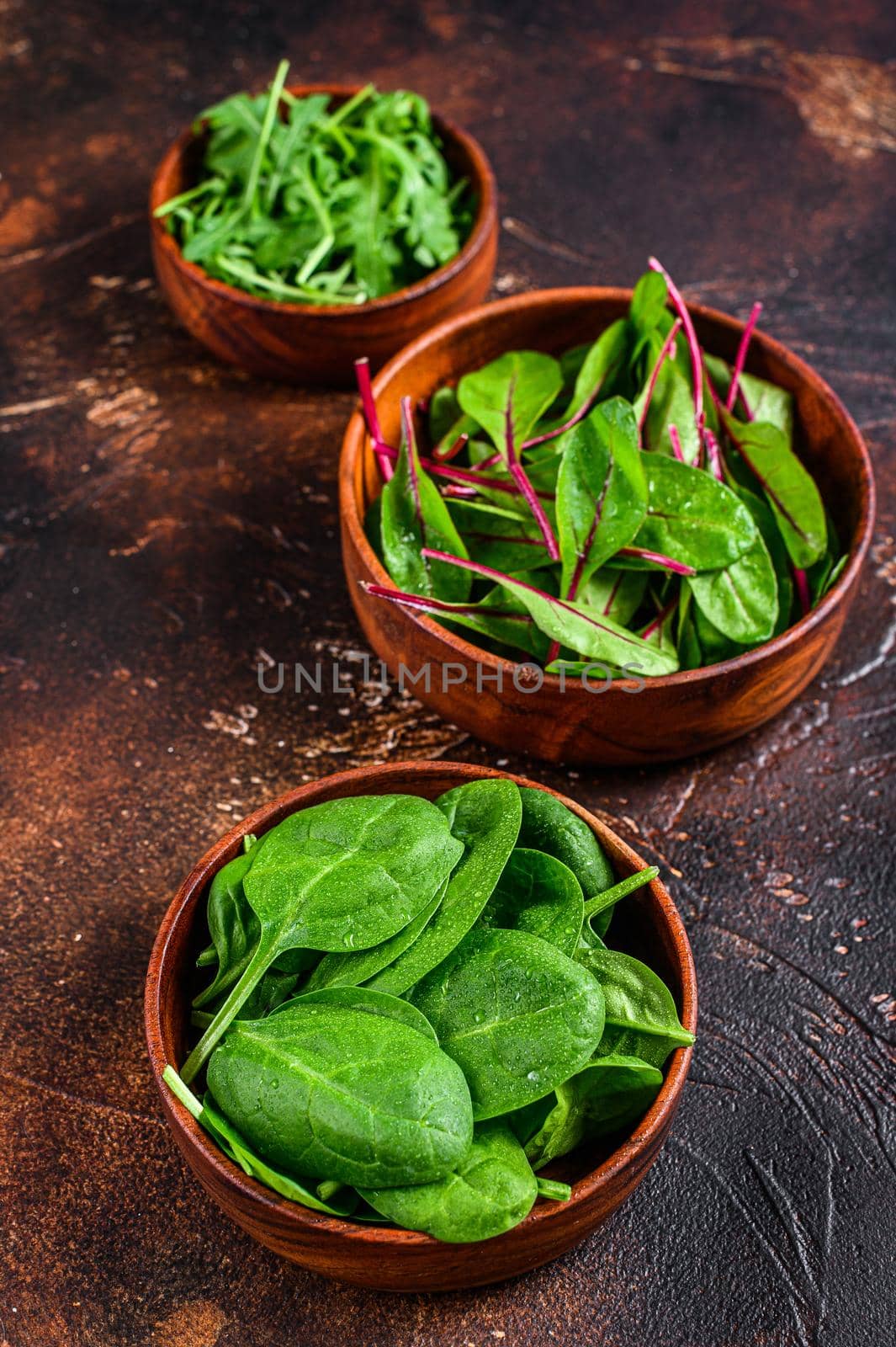 Mix Salad leafs, Arugula, Spinach and swiis Chard in wooden bowls. Dark background. Top view by Composter