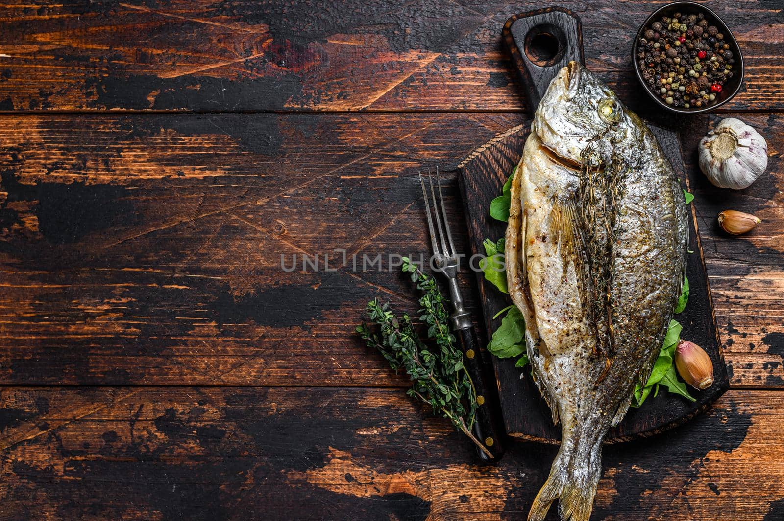 Grilled Dorada sea bream fish on a cutting board. Dark wooden background. Top view. Copy space.