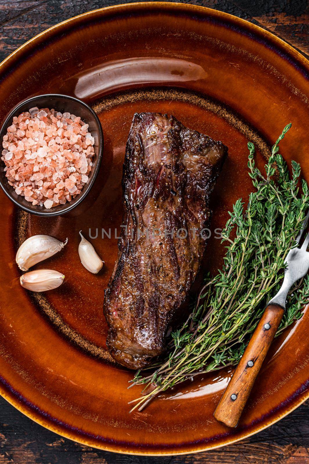 Grilled machete skirt beef steak on rustic plate with herbs and pink salt. Dark wooden background. Top view.