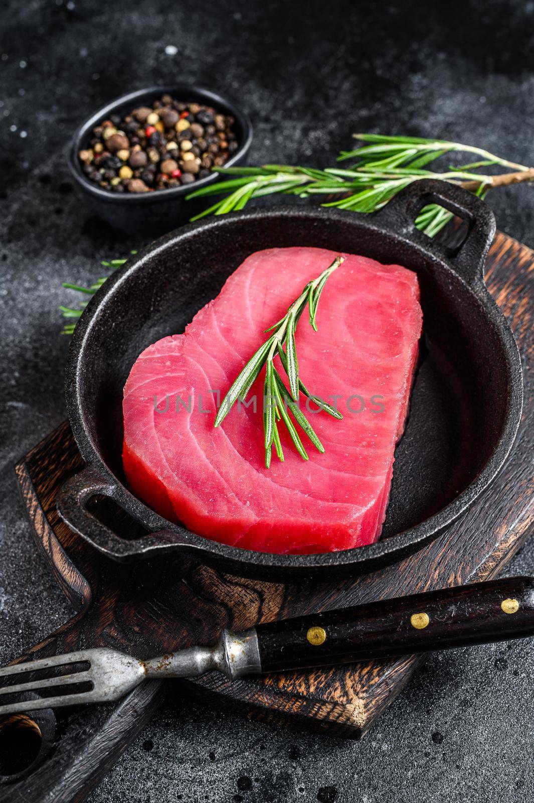 Fresh Raw tuna steak with rosemary in a pan. Black background. Top view by Composter