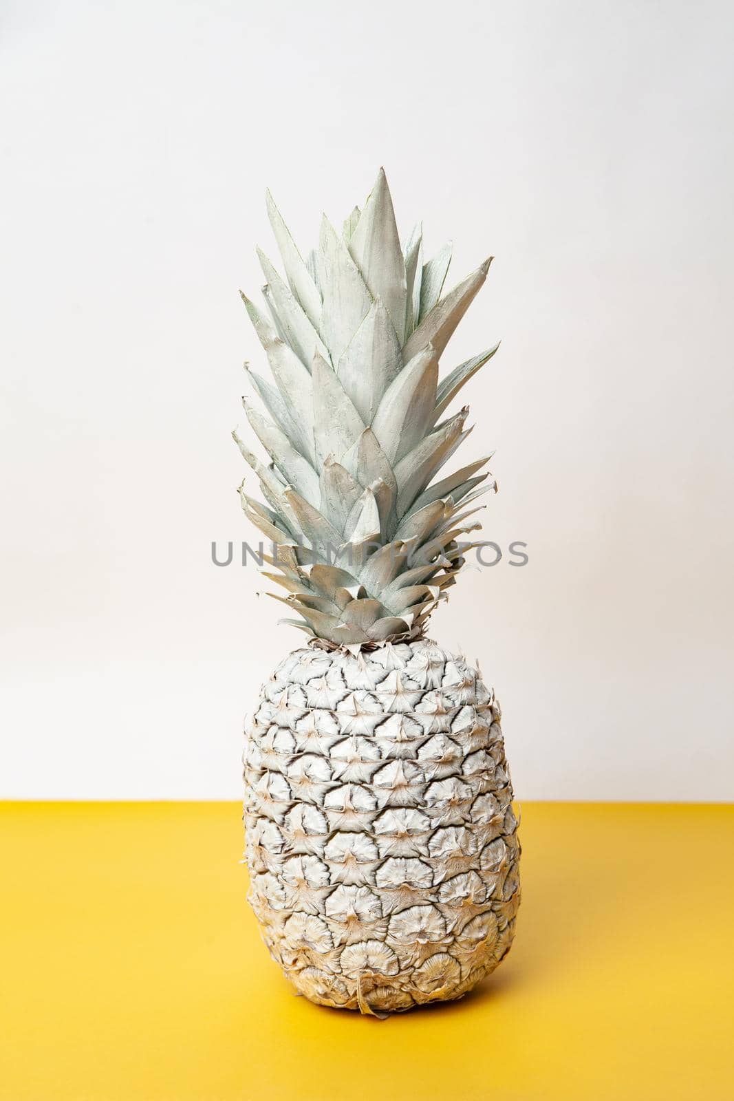 White whole fresh pineapple placed on table in modern studio on white and yellow background