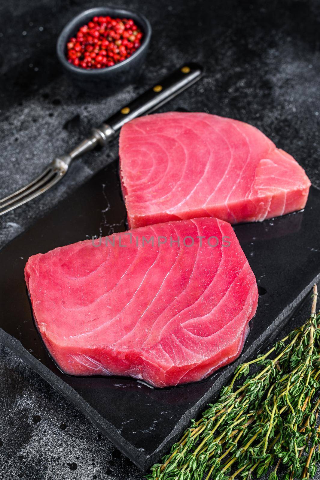 Raw tuna steak on a marble cutting Board . Black background. Top view.