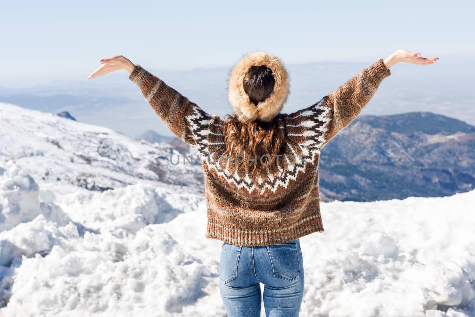 Rear view of woman enjoying the snowy mountains in winter, in Sierra Nevada, Granada, Spain. Female wearing winter clothes opening her arms.