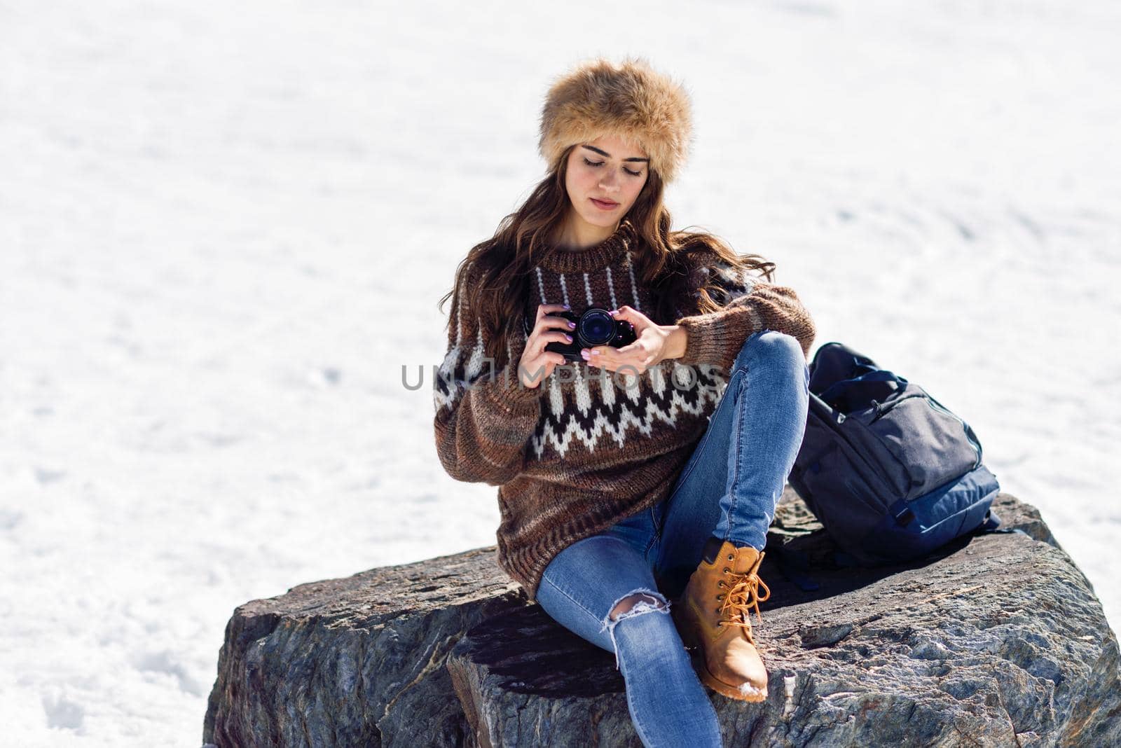 Young woman taking photographs in the snowy mountains in winter, in Sierra Nevada, Granada, Spain. Female wearing winter clothes.